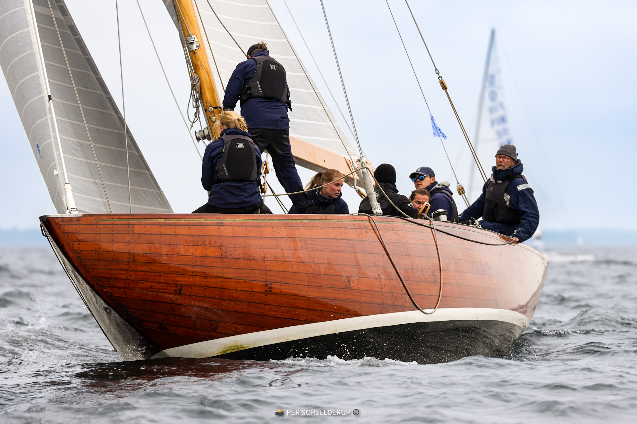 Vågspel bow-on through the chop — mahogany on wartime steel frames, still racing.